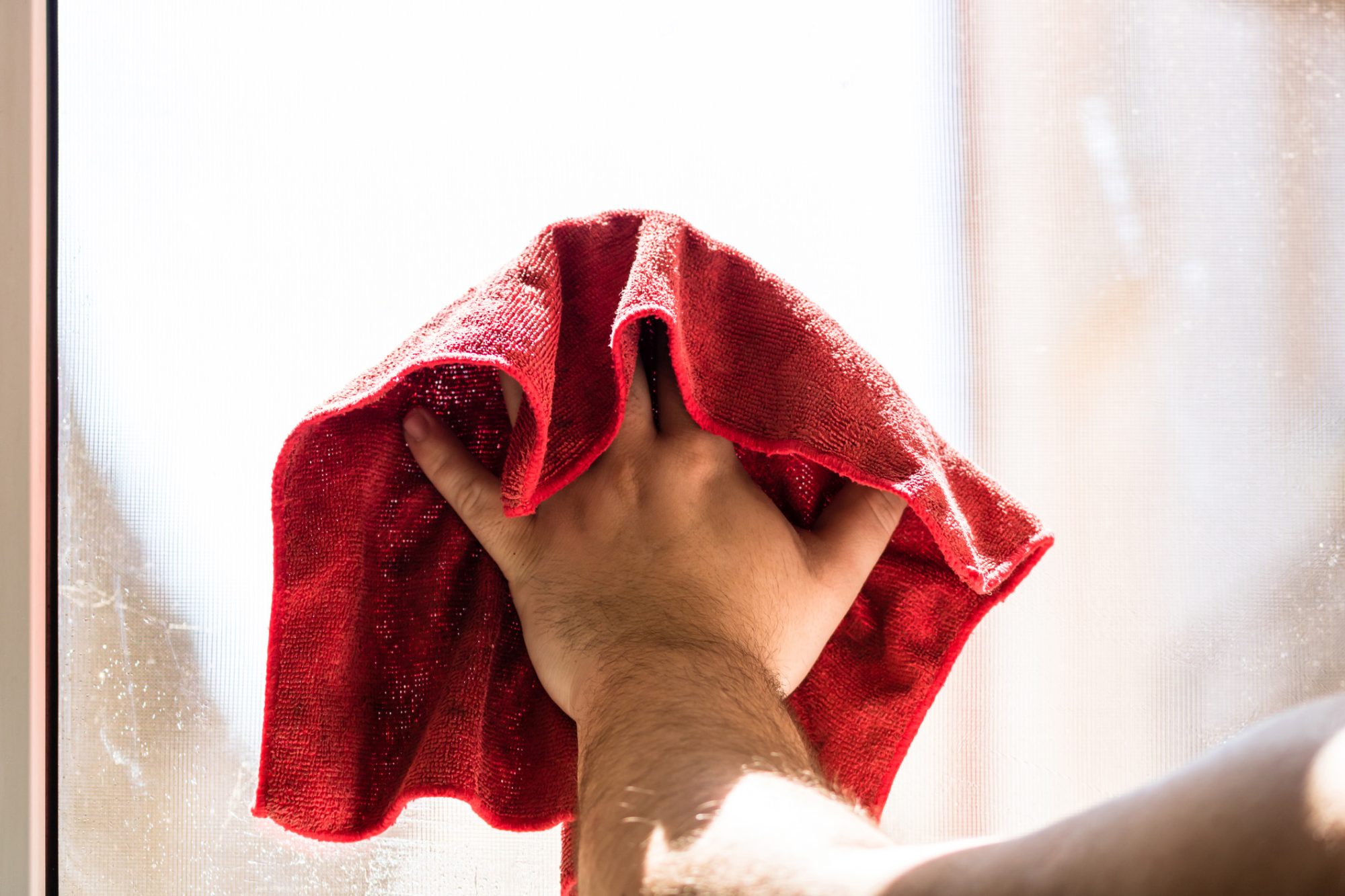 Man wiping window using red microfiber rug, cleaning services concept. Housework and housekeeping concept.